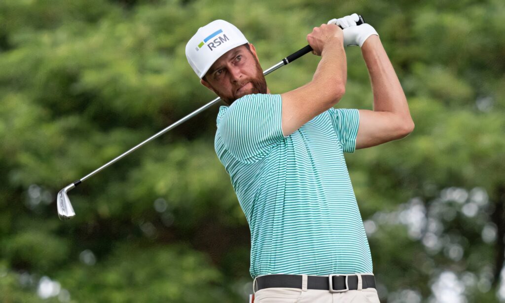Pro golfer Chris Kirk mid-swing in teal shirt and white cap on lush green golf course background Wallpaper