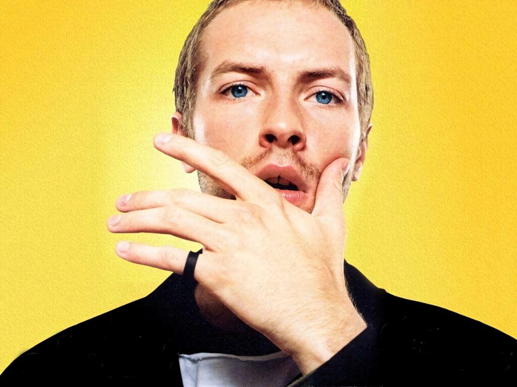 Chris Martin Coldplay close-up profile vivid yellow background blue eyes expressive hand gesture wallpaper