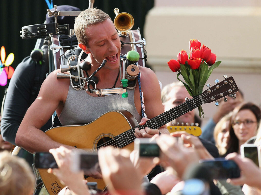 Chris Martin Coldplay performing live acoustic guitar grey tank top vibrant crowd red tulips wallpaper
