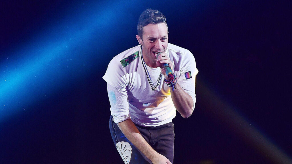 Chris Martin of Coldplay performing live on stage with vibrant blue and purple lighting energy Wallpaper