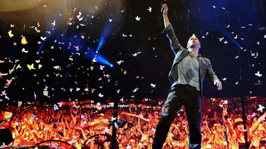 Chris Martin of Coldplay performing on stage with colorful confetti in energetic concert scene Wallpaper