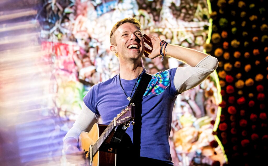 Chris Martin of Coldplay playing guitar smiling vibrant stage lighting live concert wallpaper