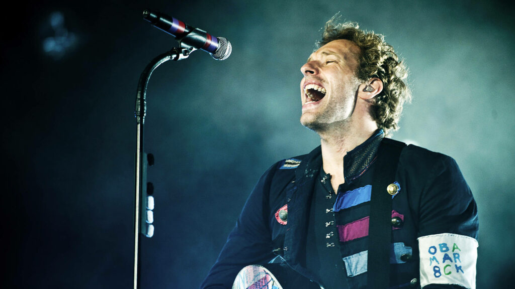 Chris Martin Coldplay vocalist passionately singing on stage vibrant energetic lights wallpaper