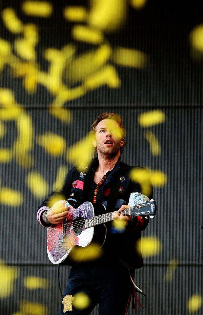 Chris Martin of Coldplay passionately performs on stage with decorated guitar and yellow confetti Wallpaper
