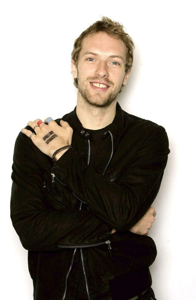 Chris Martin of Coldplay in black jacket with colorful rings and hand markings on white background Wallpaper