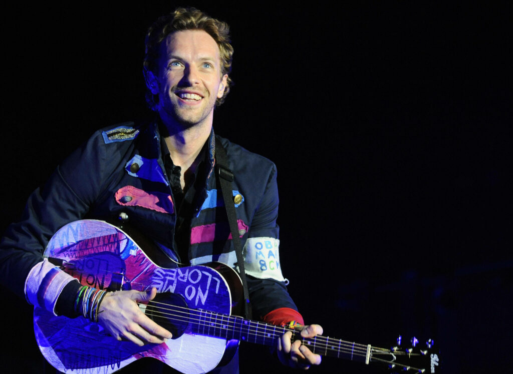 Chris Martin of Coldplay with colorful jacket and vibrant guitar on black background wallpaper