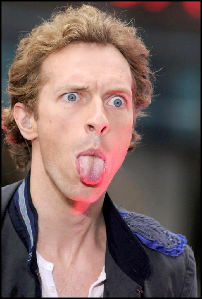 Coldplay Chris Martin goofy face with wide eyes tongue out bright lighting casual jacket fun wallpaper