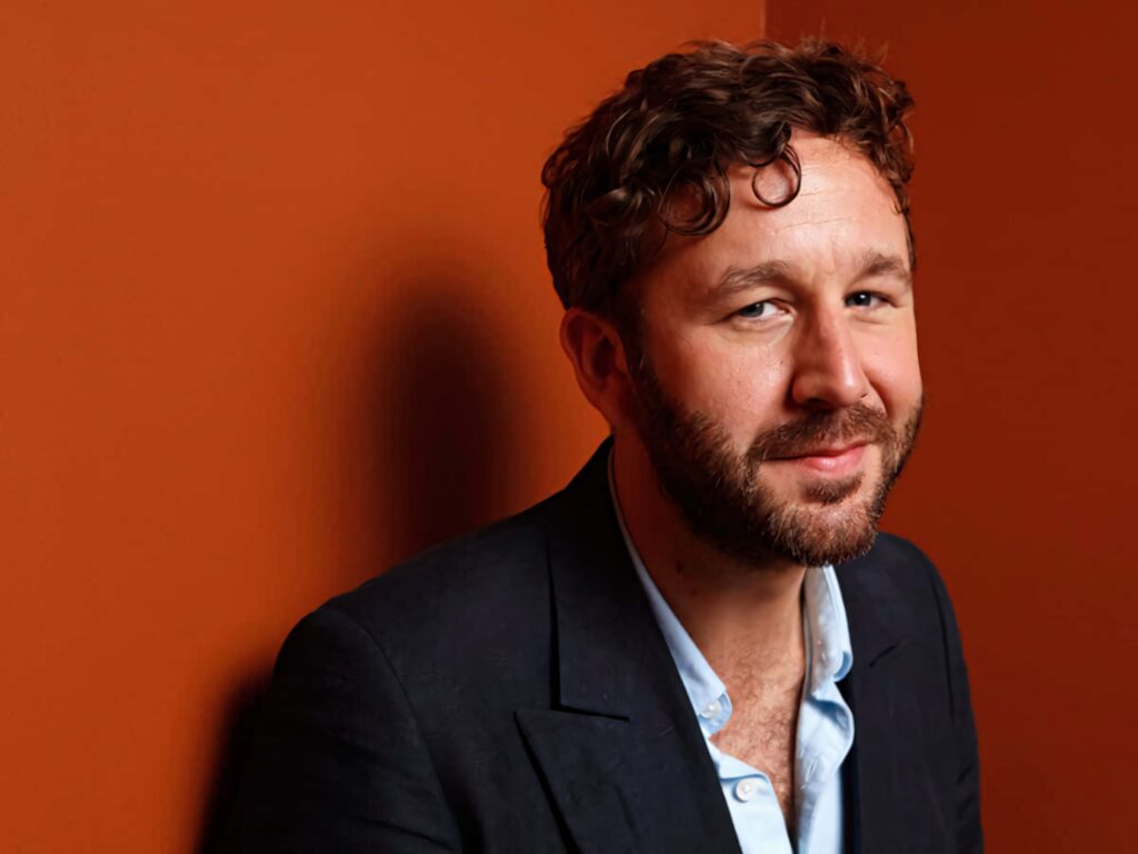 Chris O'Dowd portrait with curly hair and beard in smart casual suit on warm orange background Wallpaper
