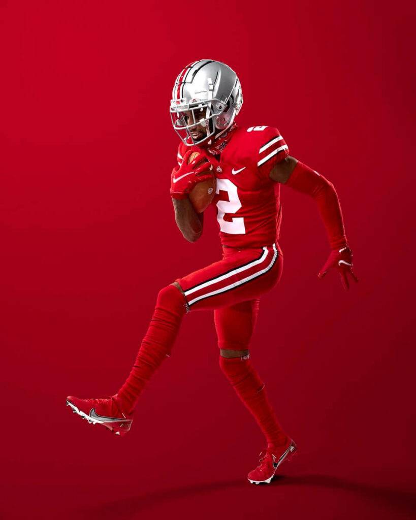 Chris Olave in red football uniform mid-action against vibrant red background sports wallpaper