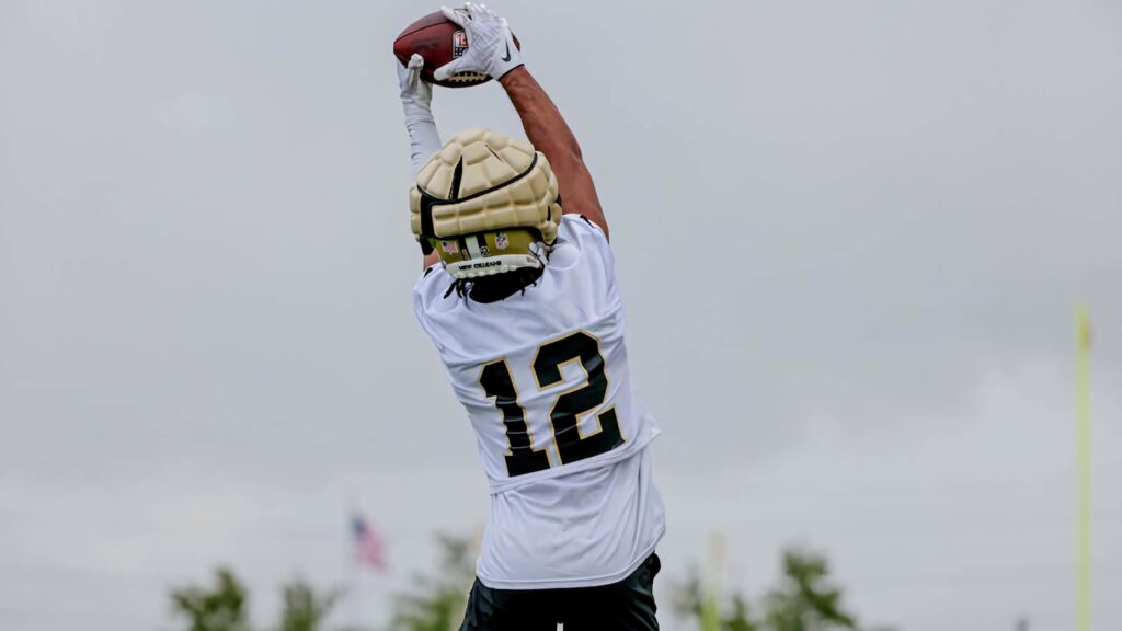Chris Olave number 12 leaps to catch football in white jersey gold helmet against cloudy sky Wallpaper