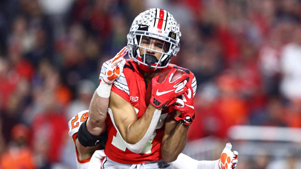 Chris Olave Ohio State receiver making intense catch in red uniform dynamic college football action Wallpaper