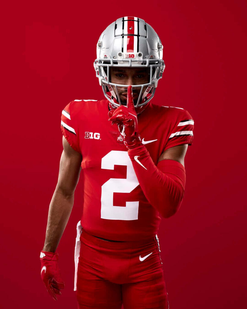 Chris Olave in red football uniform number 2 making silence gesture against bold red background Wallpaper