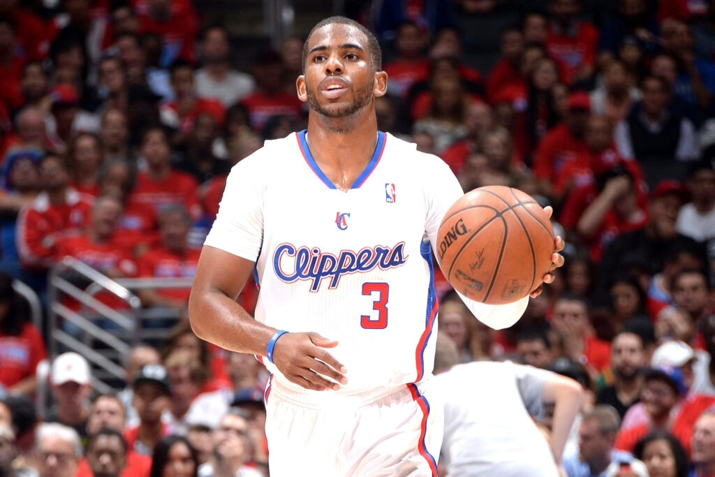 Chris Paul in white Clippers jersey dribbling basketball with intense focus NBA game action Wallpaper