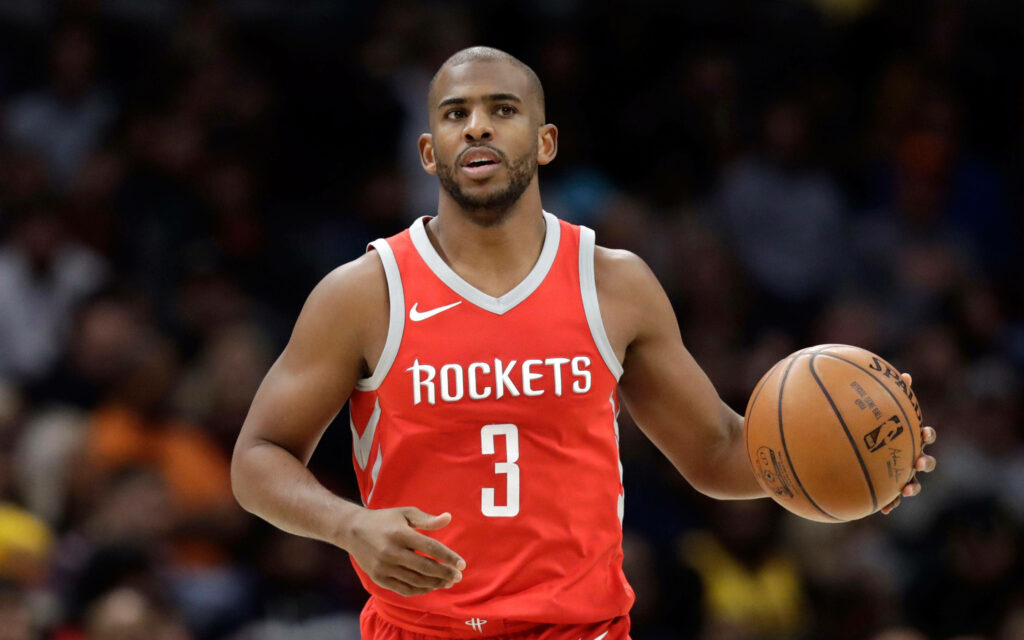 Chris Paul dribbling basketball in red Houston Rockets jersey during intense NBA game action Wallpaper