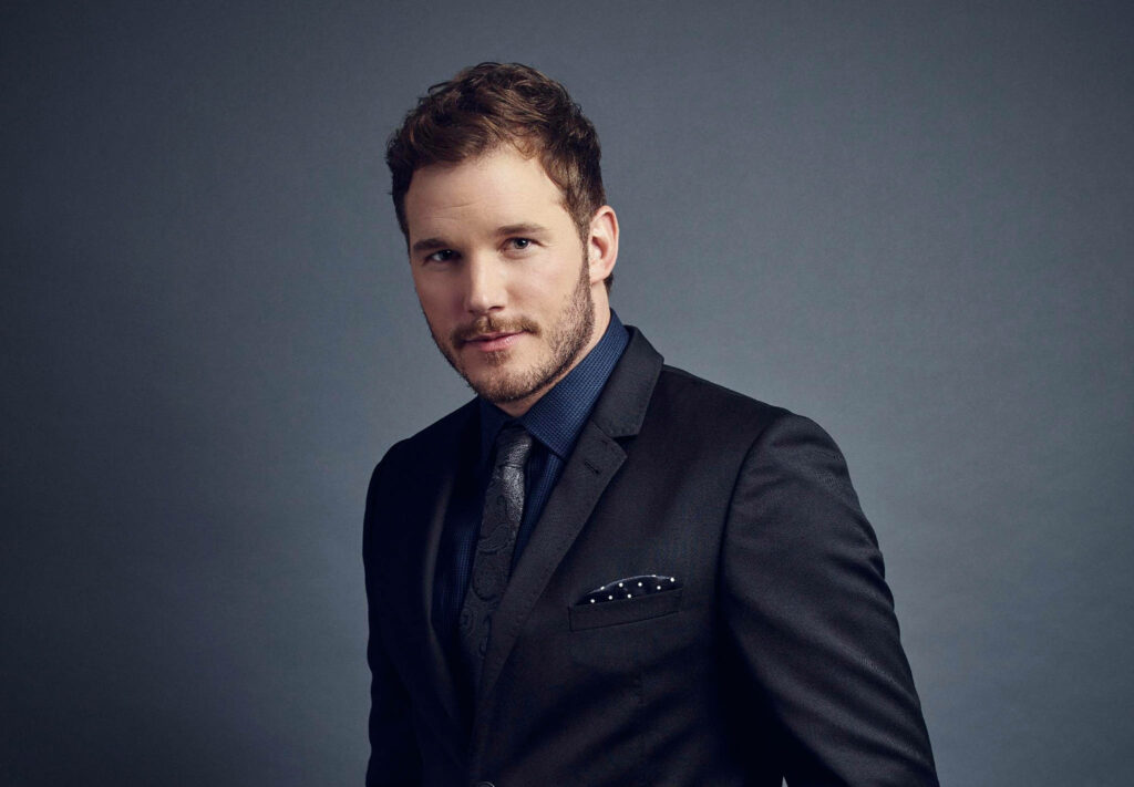 Chris Pratt in dark formal suit with sharp hair and confident pose on smooth grey background Wallpaper