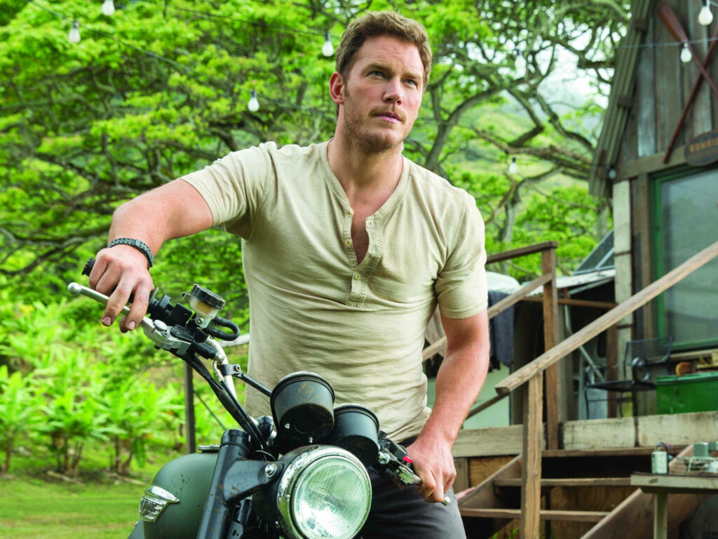 Chris Pratt leaning on rugged motorbike in lush tropical setting with vibrant green tones wallpaper