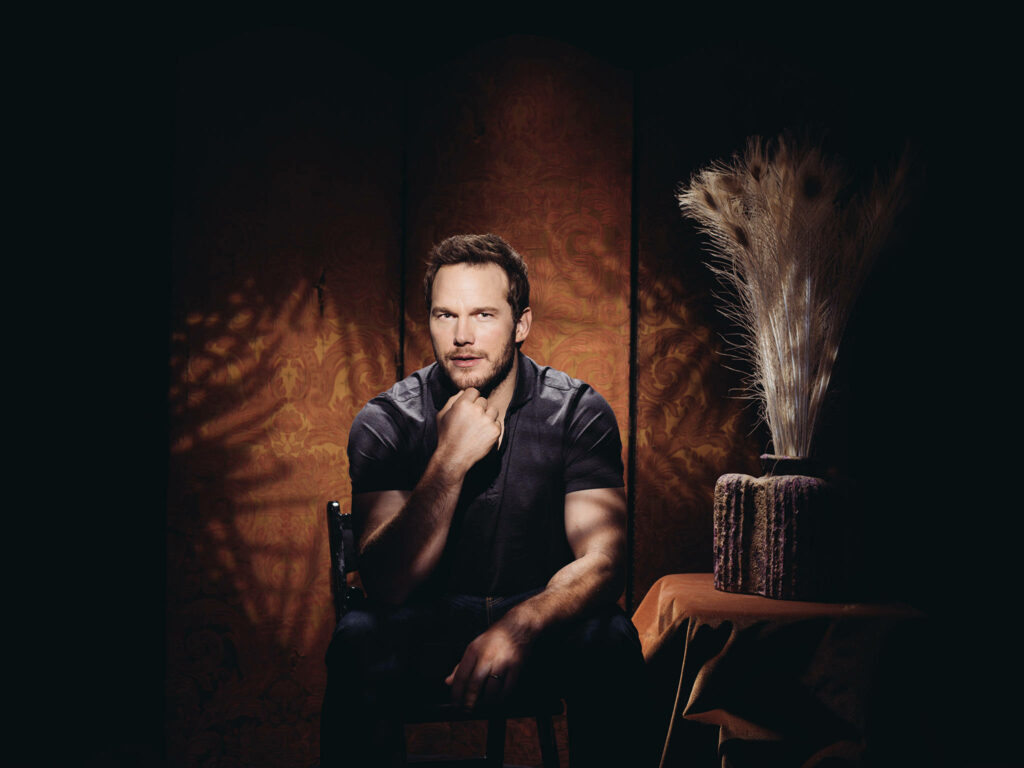 Chris Pratt seated in vintage room with ornate wallpaper textured fabrics and rustic decor accents