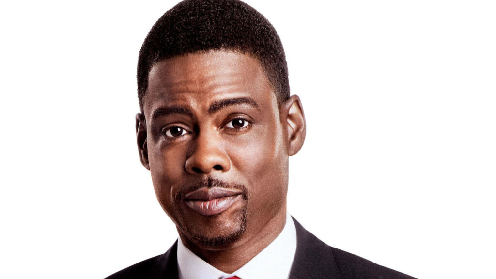 Close-up of Chris Rock in sharp suit with confident gaze on bright modern wallpaper background