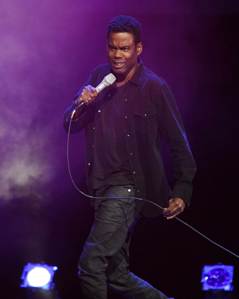 Chris Rock mid-performance holding microphone vibrant purple background energetic comedy wallpaper