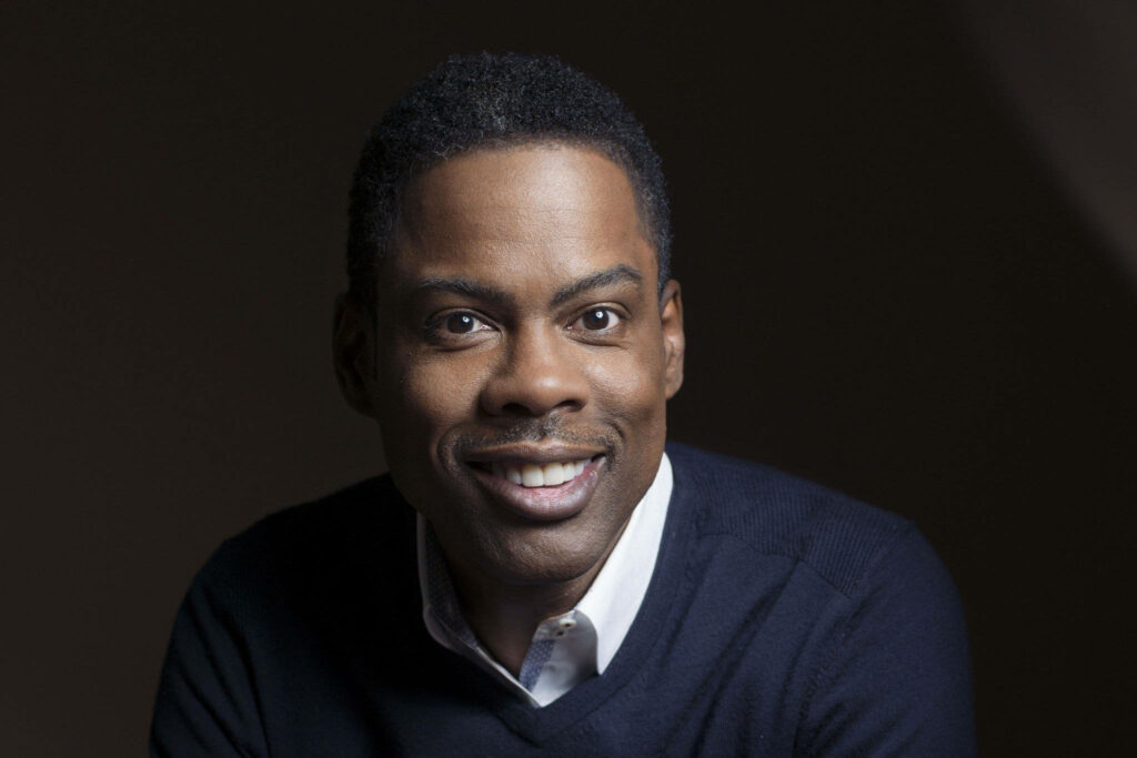 Chris Rock smiling in casual pose on dark background vibrant wallpaper for comedian fans