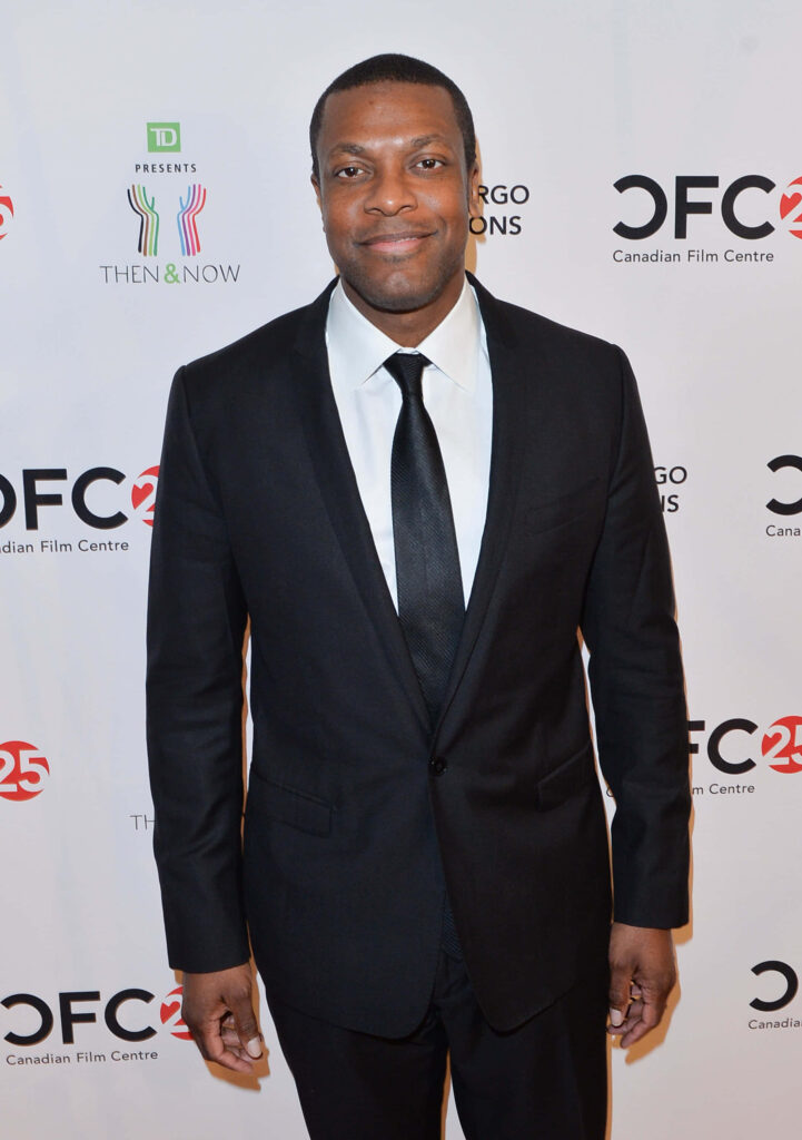 Chris Tucker in sharp black suit and tie standing confidently at white event backdrop wallpaper