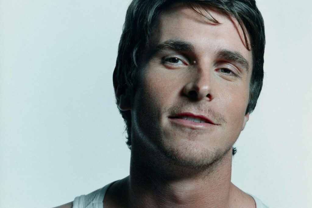 Close-up of Christian Bale with subtle smile on light background showcasing expressive features Wallpaper