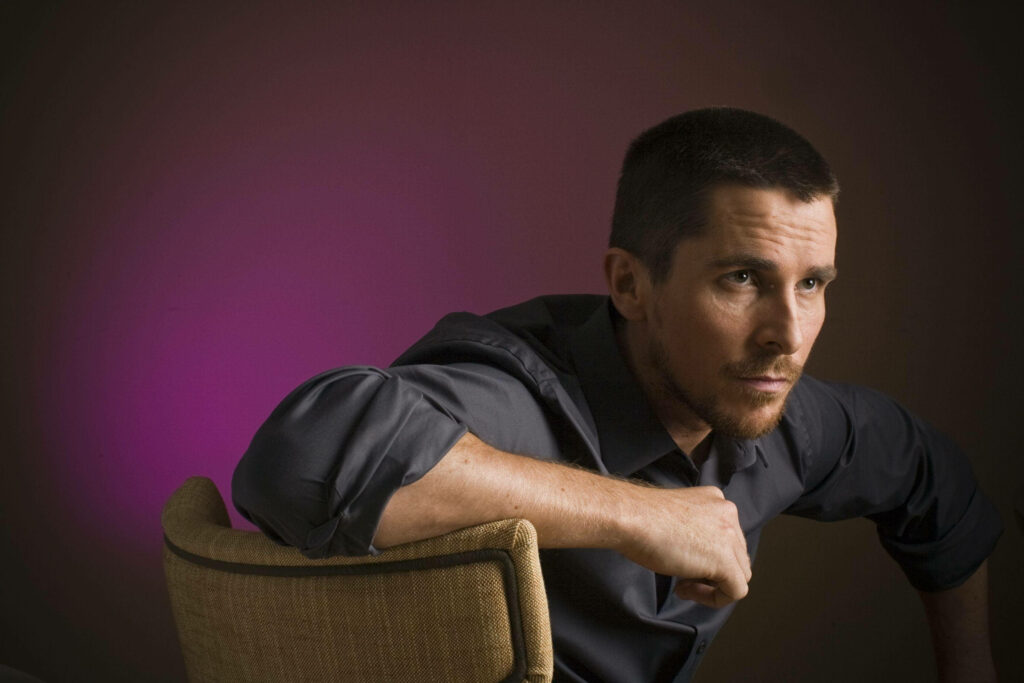 Christian Bale seated thoughtfully with purple backdrop intense contemplative portrait wallpaper