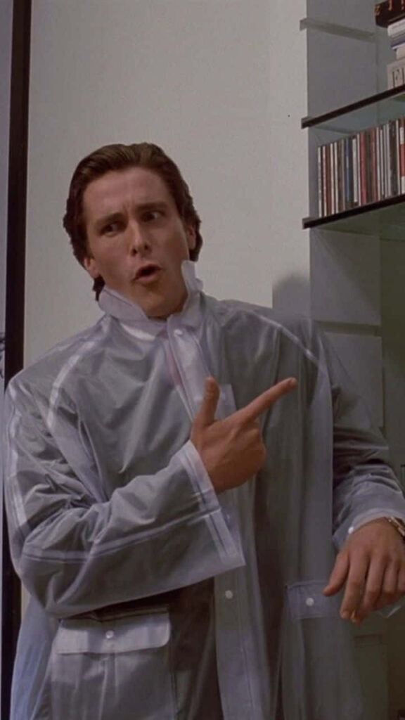 Christian Bale as Patrick Bateman in clear raincoat making gun gesture high definition wallpaper