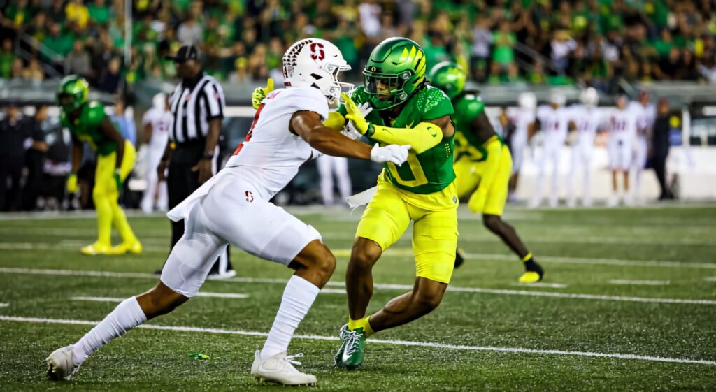 Christian Gonzalez football action in bright yellow and green uniform blocking opponent under lights Wallpaper