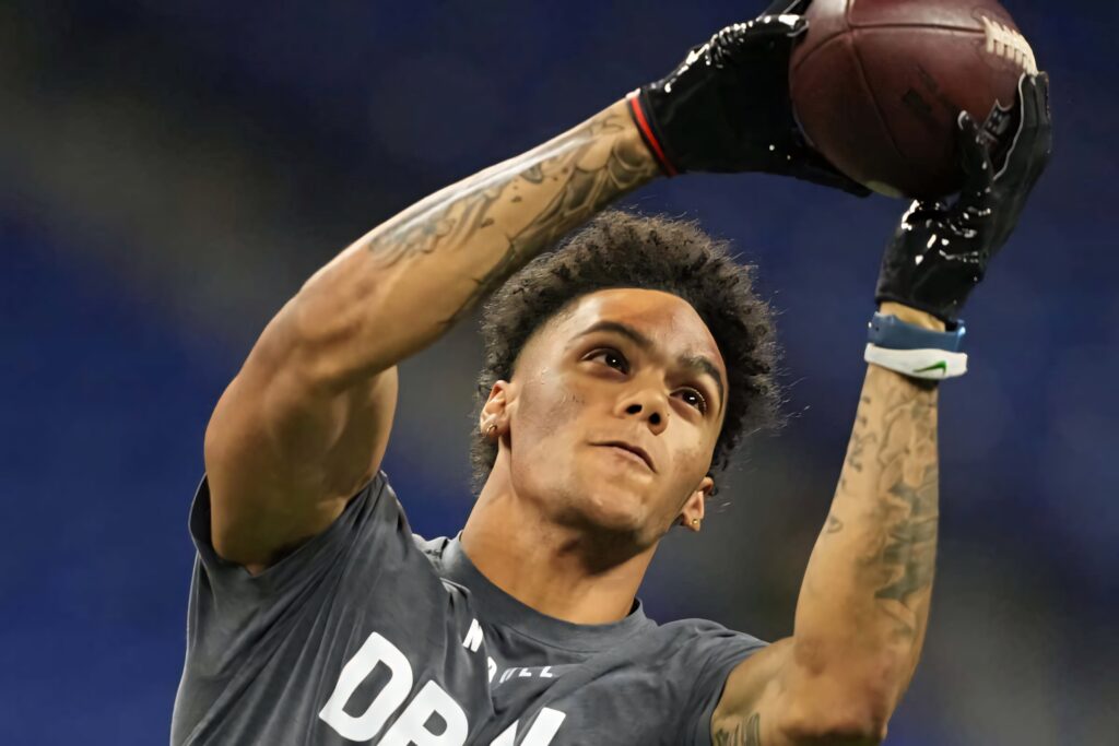 Christian Gonzalez midair catching football intense action tattooed arms athletic physique blue background Wallpaper