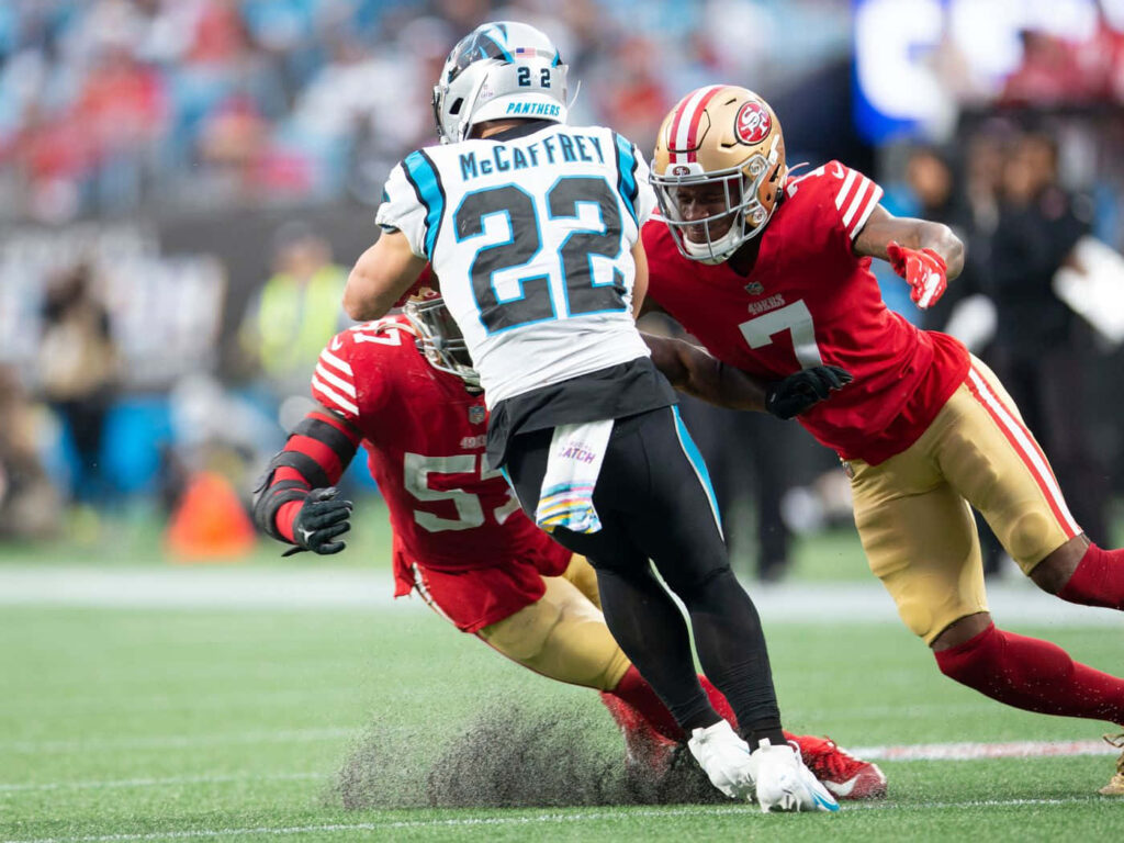 Christian McCaffrey running with football against 49ers defenders on vibrant football field wallpaper