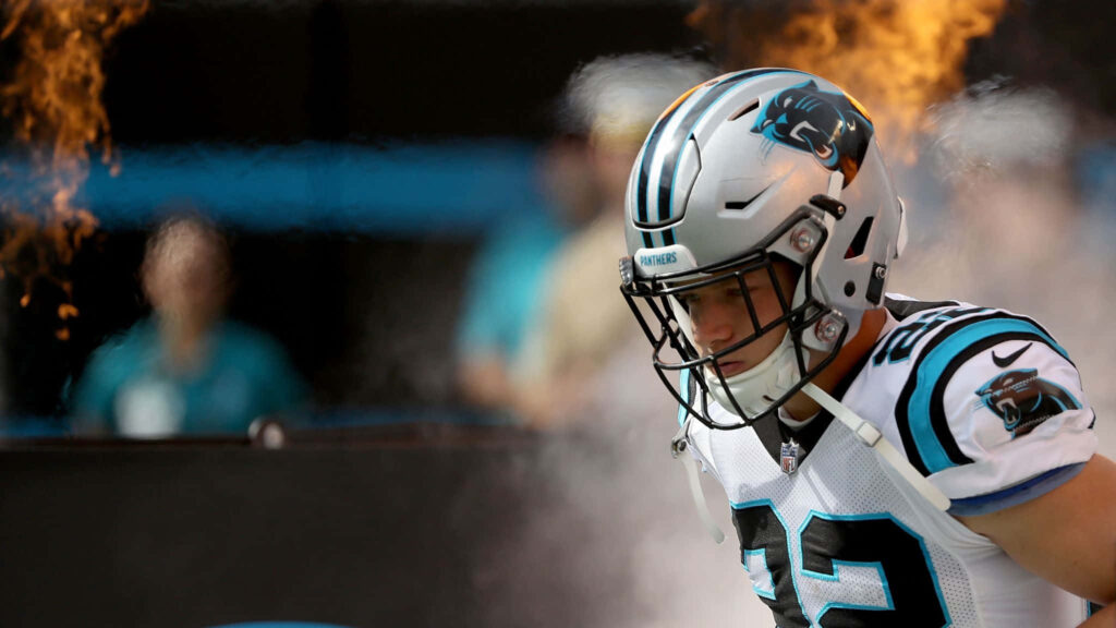 Christian McCaffrey in Carolina Panthers gear emerging through smoke and fire ready to play Wallpaper
