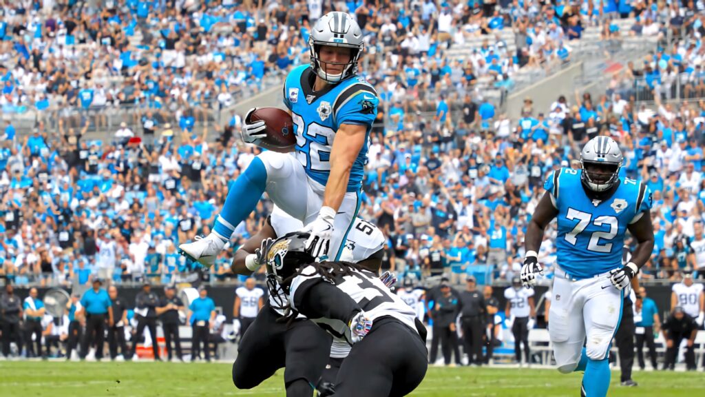 Christian McCaffrey leaps over defender in Carolina Panthers NFL game with vibrant stadium fans Wallpaper