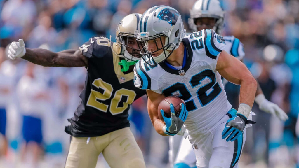 Christian McCaffrey runs with football for Carolina Panthers versus New Orleans Saints defender on field Wallpaper