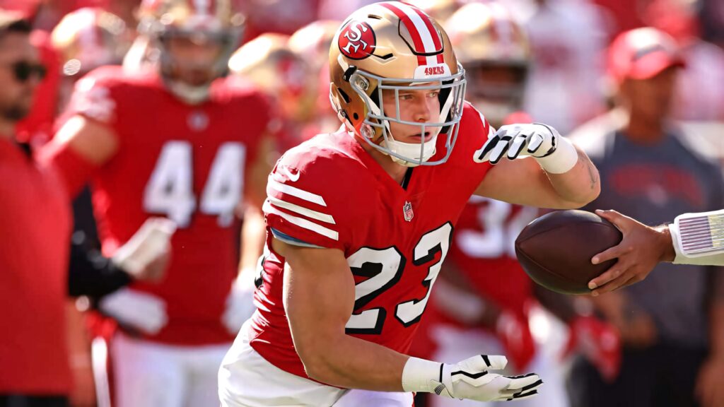 Christian McCaffrey in red 49ers uniform sprinting on field with dynamic stadium background wallpaper