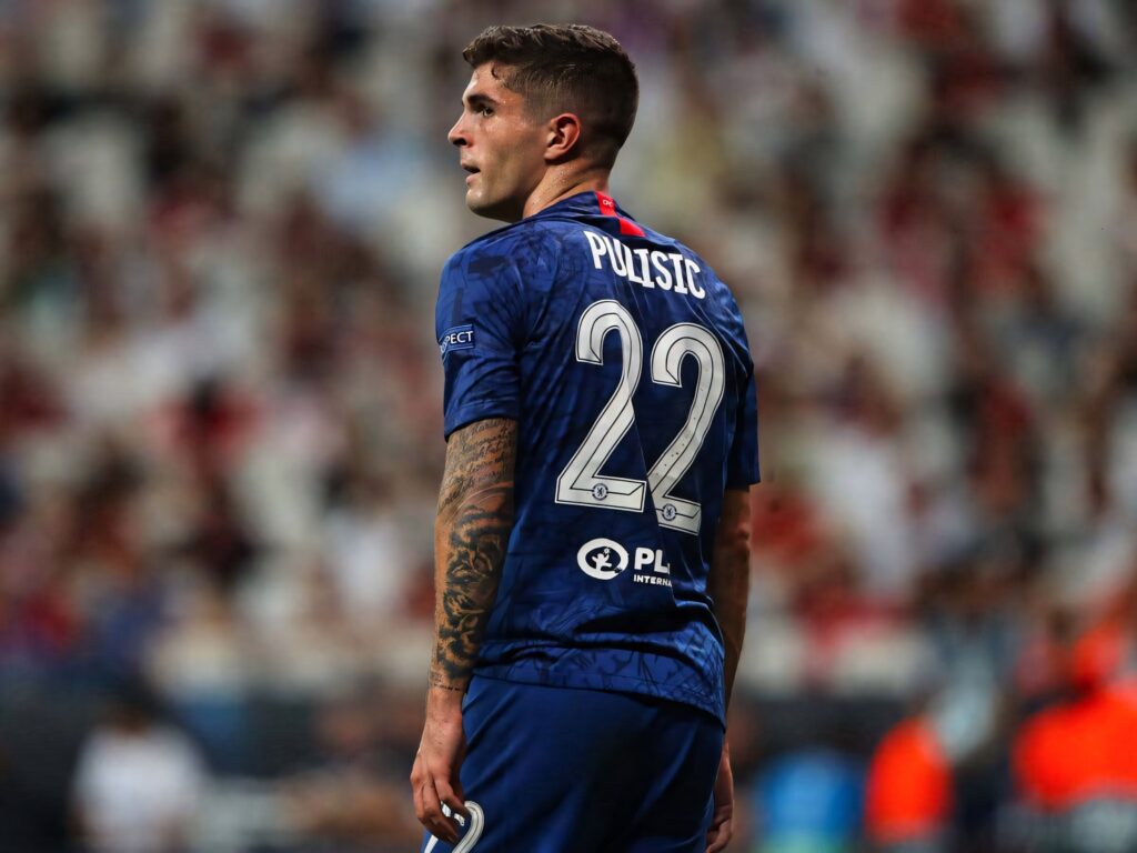 Christian Pulisic in blue Chelsea jersey number 22 focused during intense soccer match with tattoos visible Wallpaper