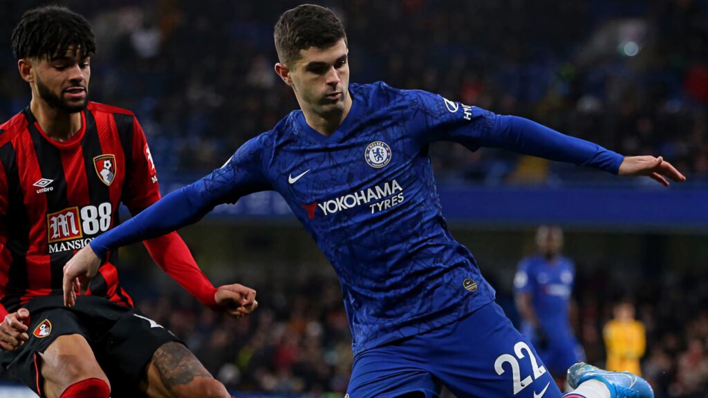 Christian Pulisic in Chelsea blue kit stretches arms wide in dynamic football action stadium scene Wallpaper