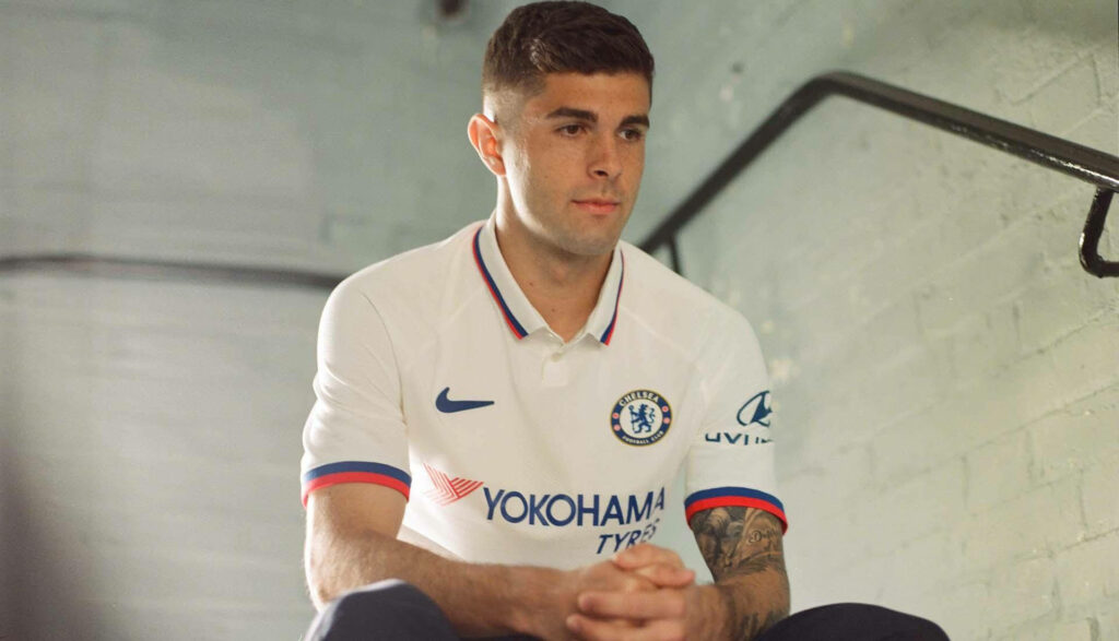 Christian Pulisic sitting on stairs wearing Chelsea FC jersey with focused expression and soft lighting Wallpaper