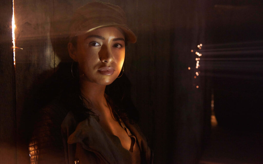 Christian Serratos in rugged jacket and cap with dramatic light rays cinematic moody wallpaper background
