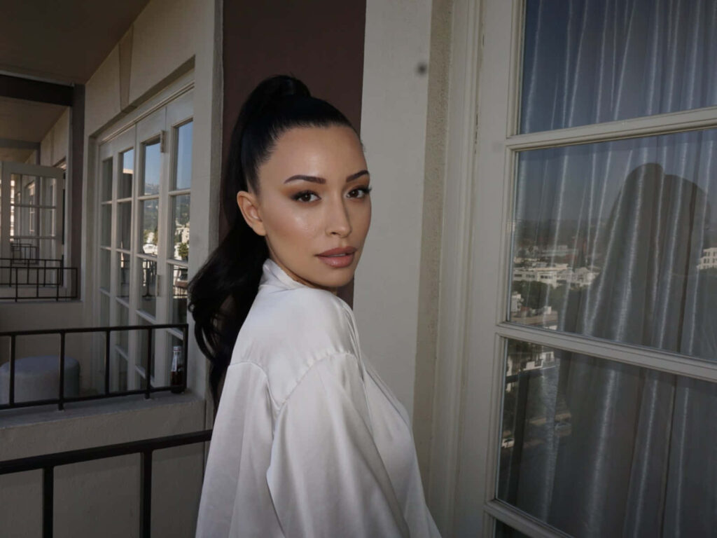 Christian Serratos in ivory satin robe on balcony with city views soft natural light elegant look Wallpaper