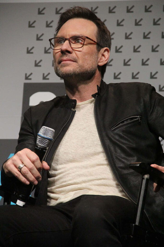 Christian Slater in casual cream shirt and black leather jacket against geometric background wallpaper