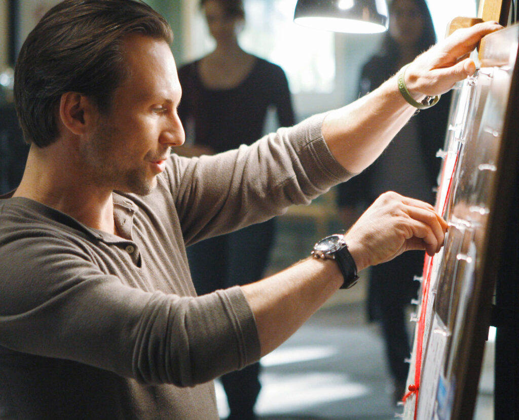 Christian Slater focused on crime investigation board in warm light thriller detective wallpaper background