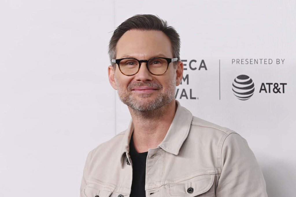 Christian Slater in beige jacket and dark shirt on white background minimalist portrait wallpaper