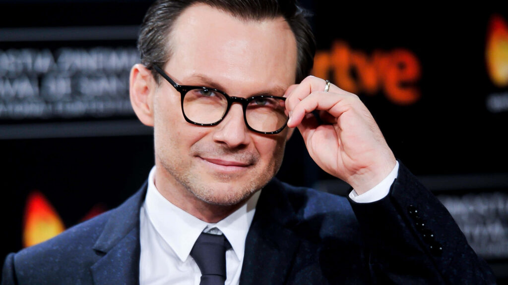 Christian Slater in dark suit and glasses with confident smile in modern professional setting wallpaper