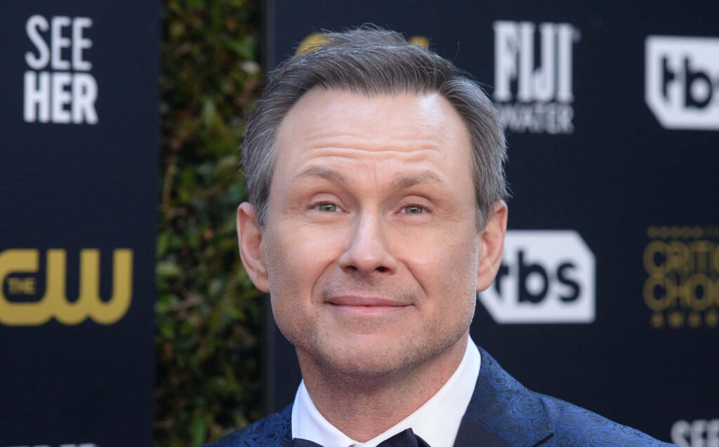Christian Slater in blue patterned suit posing confidently at event backdrop wallpaper