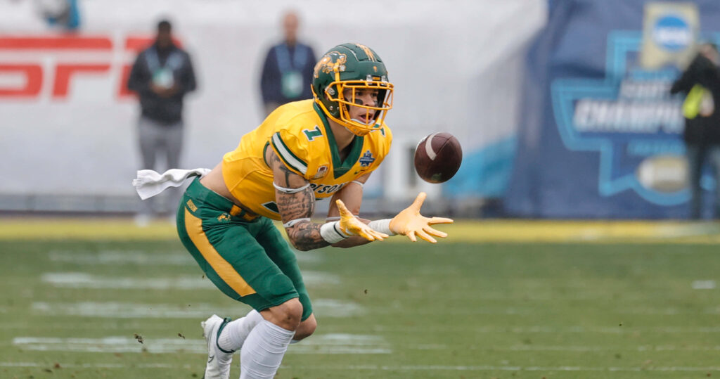 Christian Watson in green and yellow uniform catching football during intense game action wallpaper