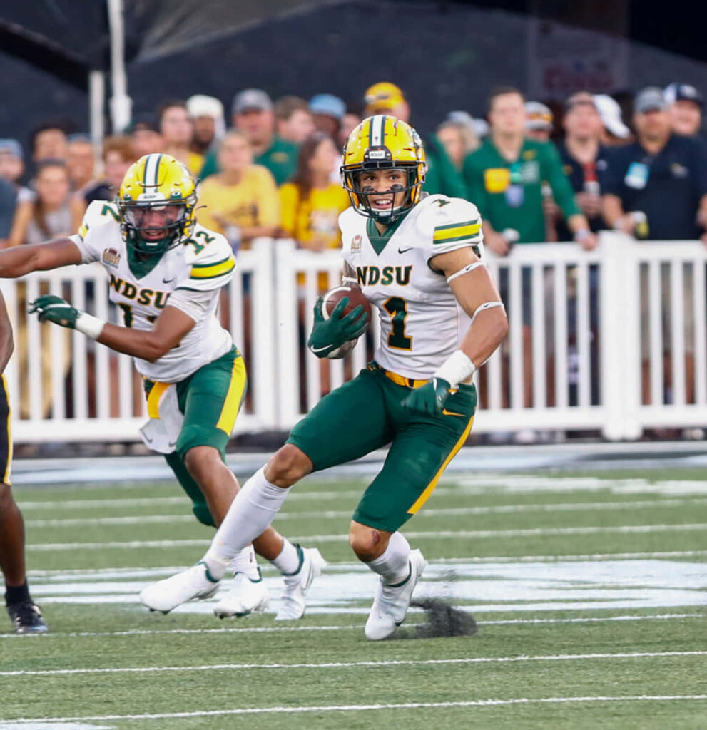 Christian Watson NDSU football player running with ball in green gold uniform stadium background Wallpaper