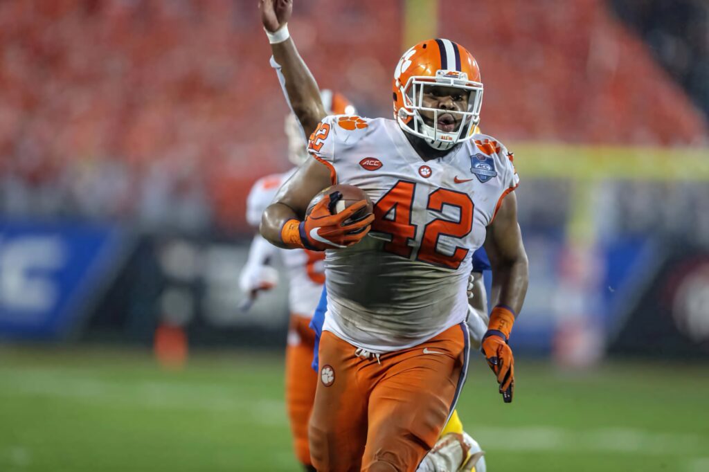 Clemson Christian Wilkins in vibrant orange and white celebrating intense football game action background Wallpaper