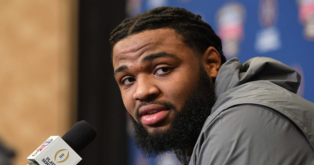 Christian Wilkins at press conference focused expression blue backdrop sports event logos Wallpaper