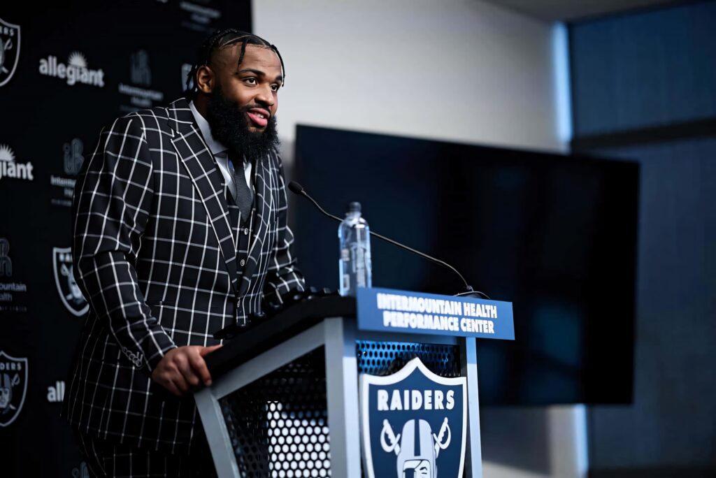 Christian Wilkins in checkered suit at Raiders press conference with logo backdrop and sponsors Wallpaper